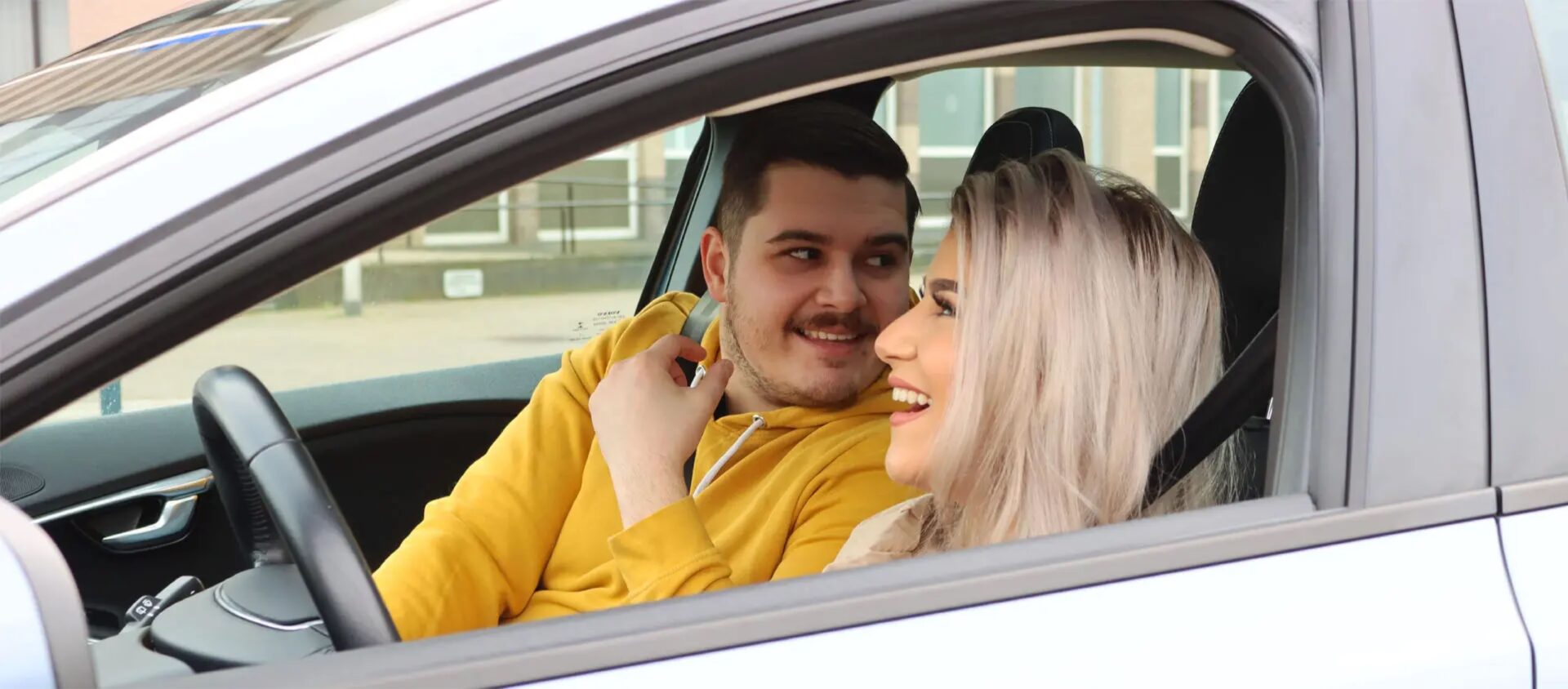 Rijinstructeur en leerling lachen samen in een rijschoolauto tijdens een les
