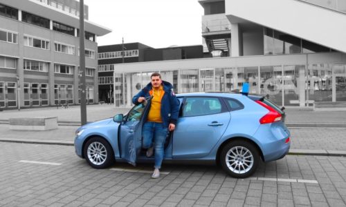 Man stapt uit lesauto met rijschoolbord op het dak in een stedelijke omgeving